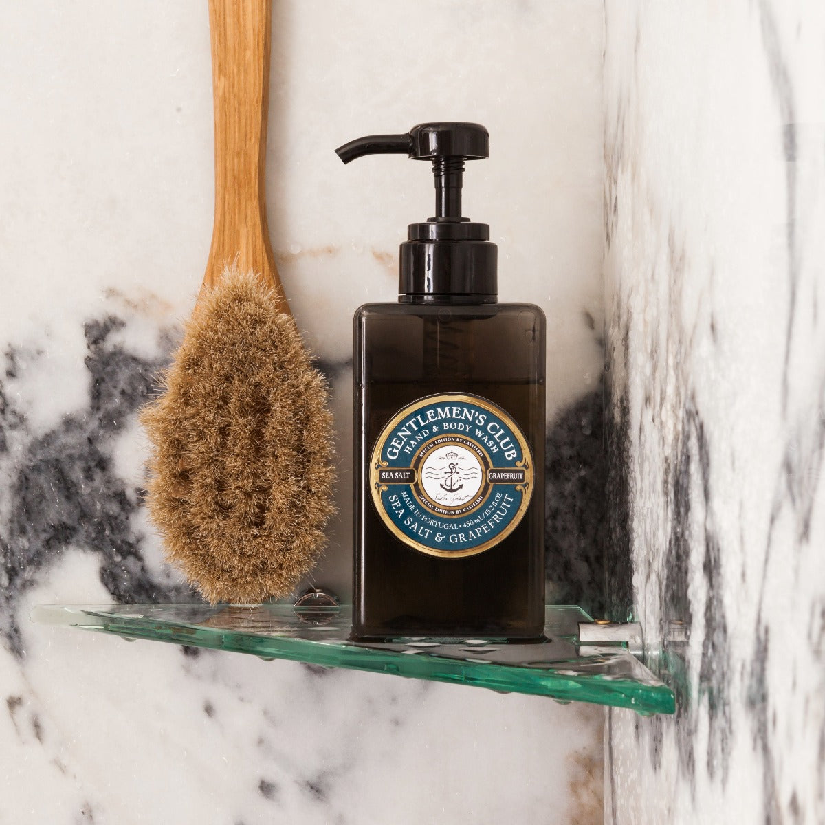 Gentlemen's Club' Sea Salt And Grapefruit Luxury Hand And Body Wash - Brown Bottle Dispenser with decorative Blue & Brown Gift Box - Lifestyle image of a Hand & Body Wash botlle in the shower alongside a shower brush.