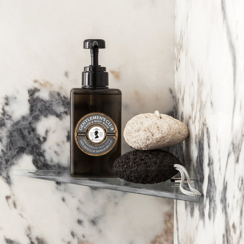 Gentlemen's Club Patchouli And Sandalwood Luxury Hand & Body Wash - Lifestyle image Bottle in the shower next to two pumice stones