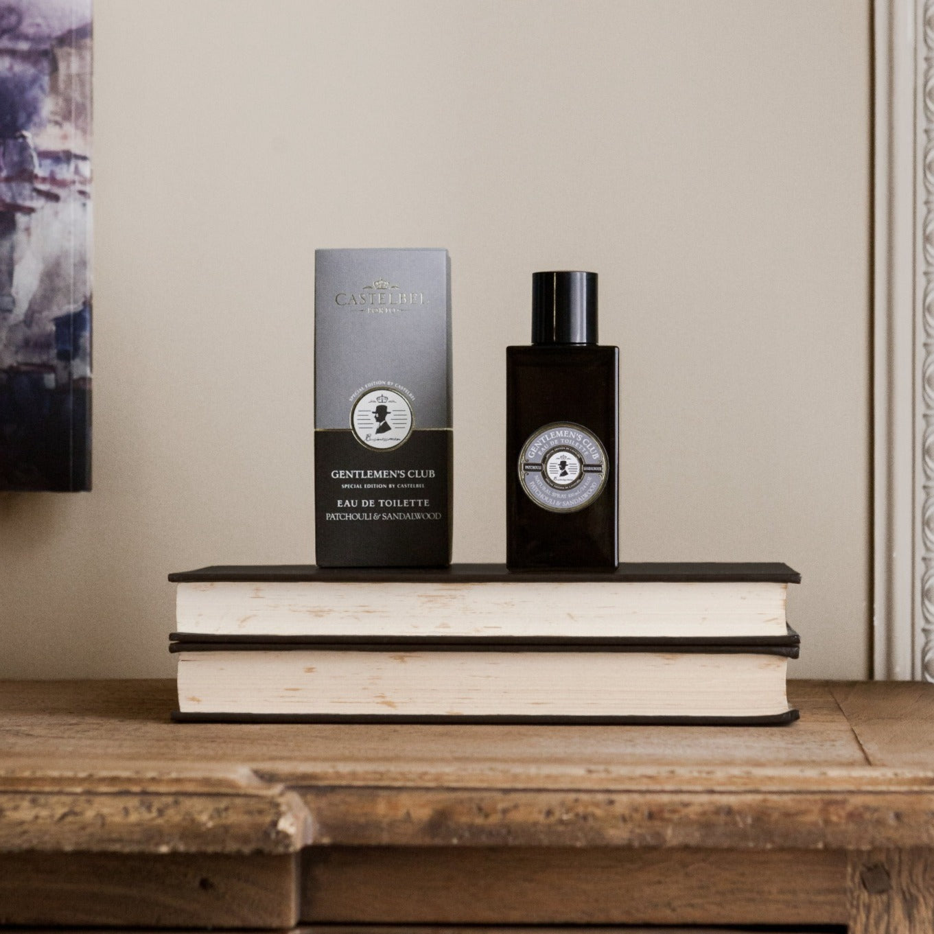 Gentlemen's Club' Patchouli & Sandalwood Eau De Toilette - Gift for men - A grey bottle with a grey and brown gift box. Lifestyle image of the perfume stood on two books.