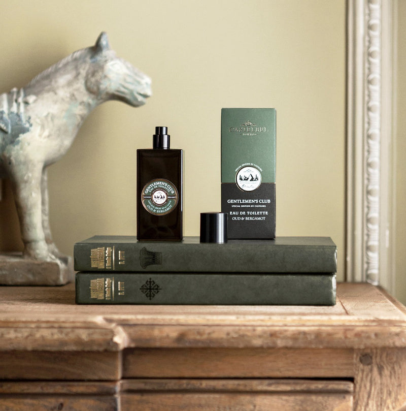 'Gentleman's Club' Oud & Bergamot Eau De Toilette  - Brown bottle with a decorative Green and Brown gift box - Lifestyle image showing the 'eau de toilette' on a stack on books